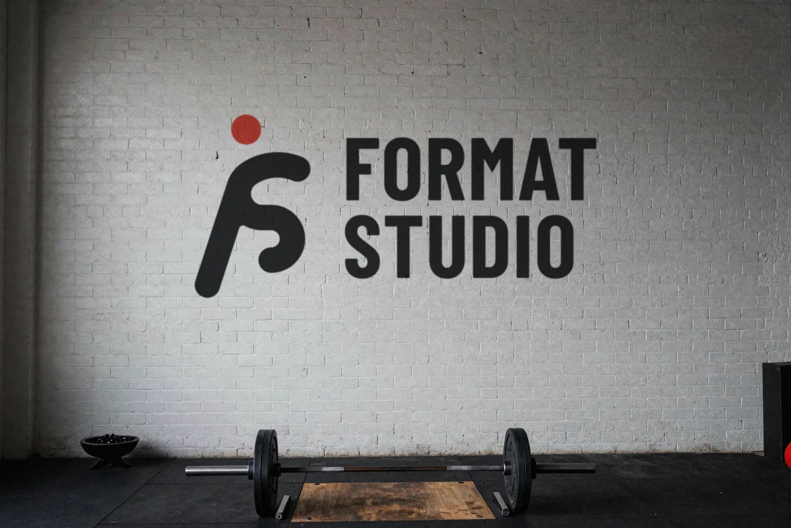 The Format Studio logo painted on a white brick wall inside the studio, above a loaded barbell on a lifting platform
