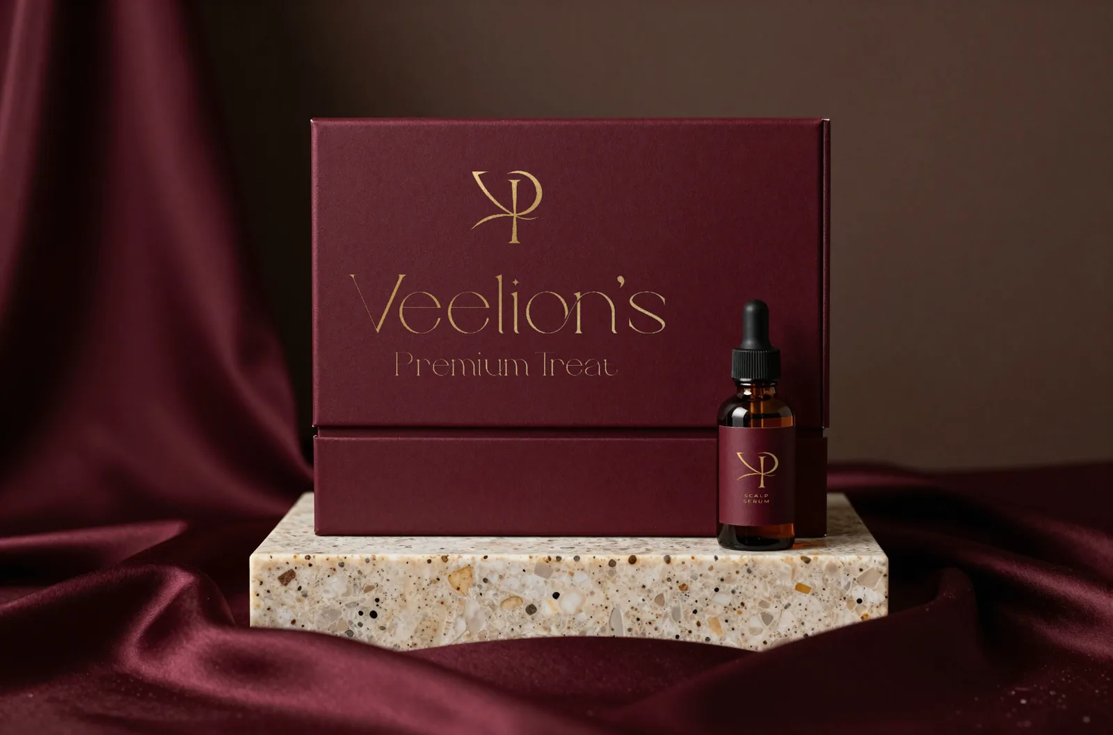 Burgundy Veelion's gift box with the gold foil lockup and a matching serum bottle on a stone plinth